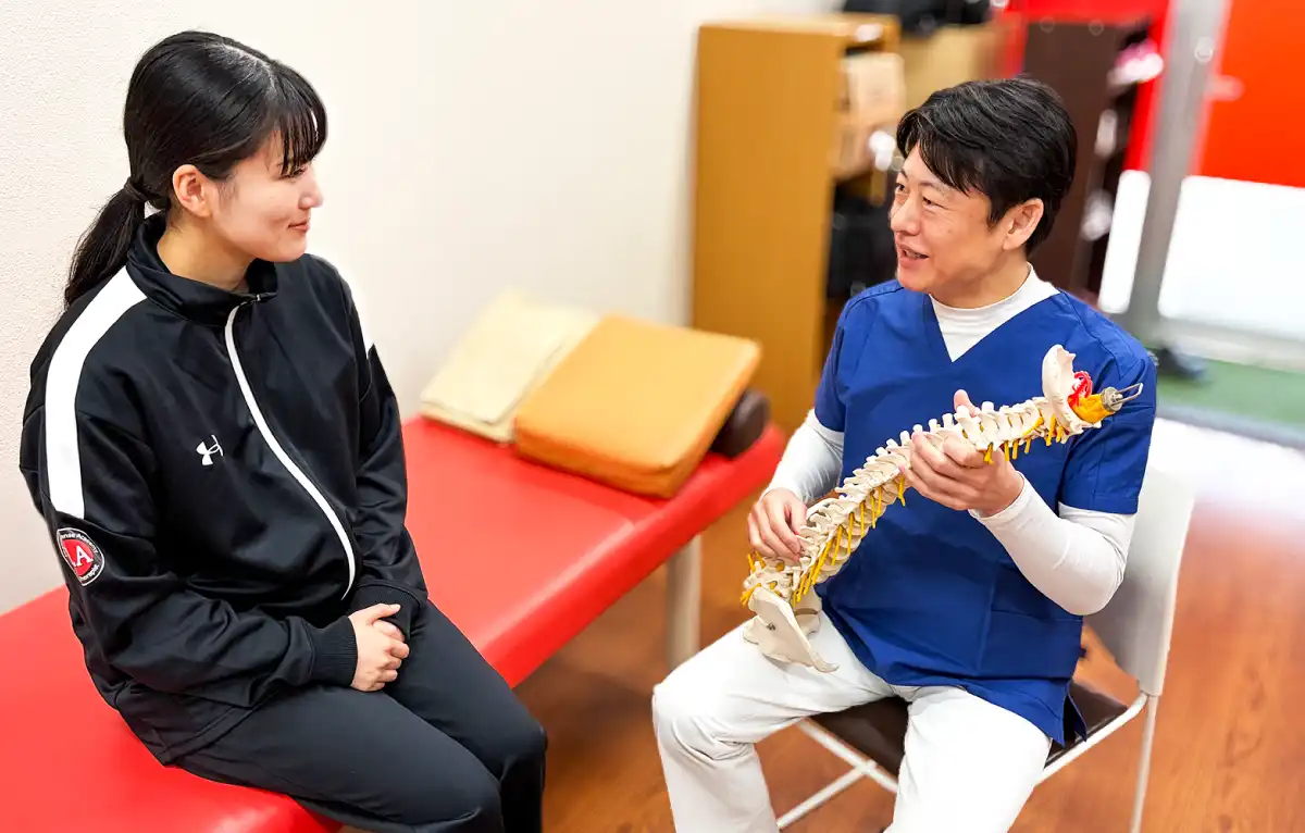 宮下先生が背骨の模型を持って女性の患者にアドバイスしている写真
